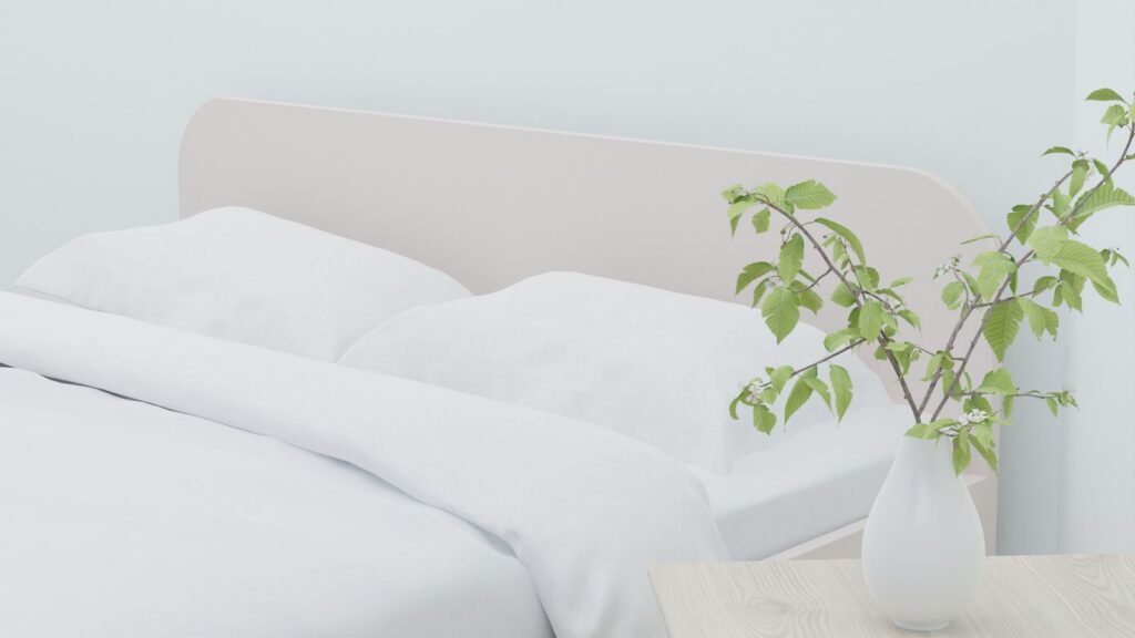 A bright bedroom with white bedding and a green sprig in a vase