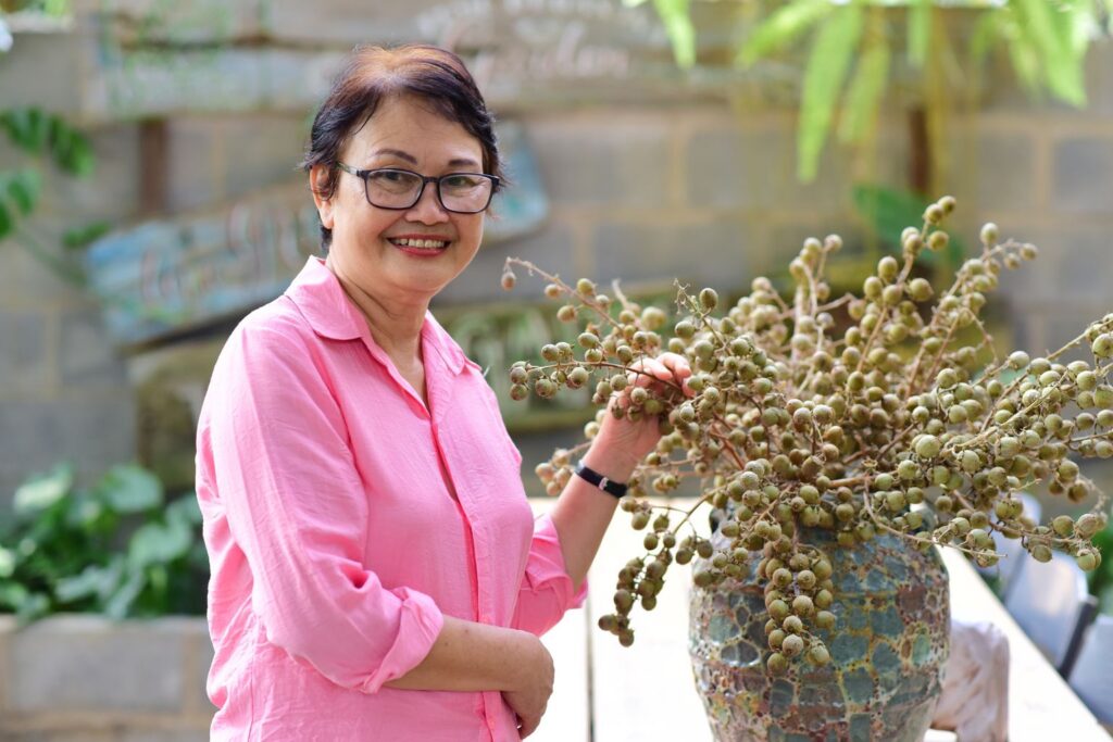 A smiling woman in her fifties in a pink shirt tending her plants