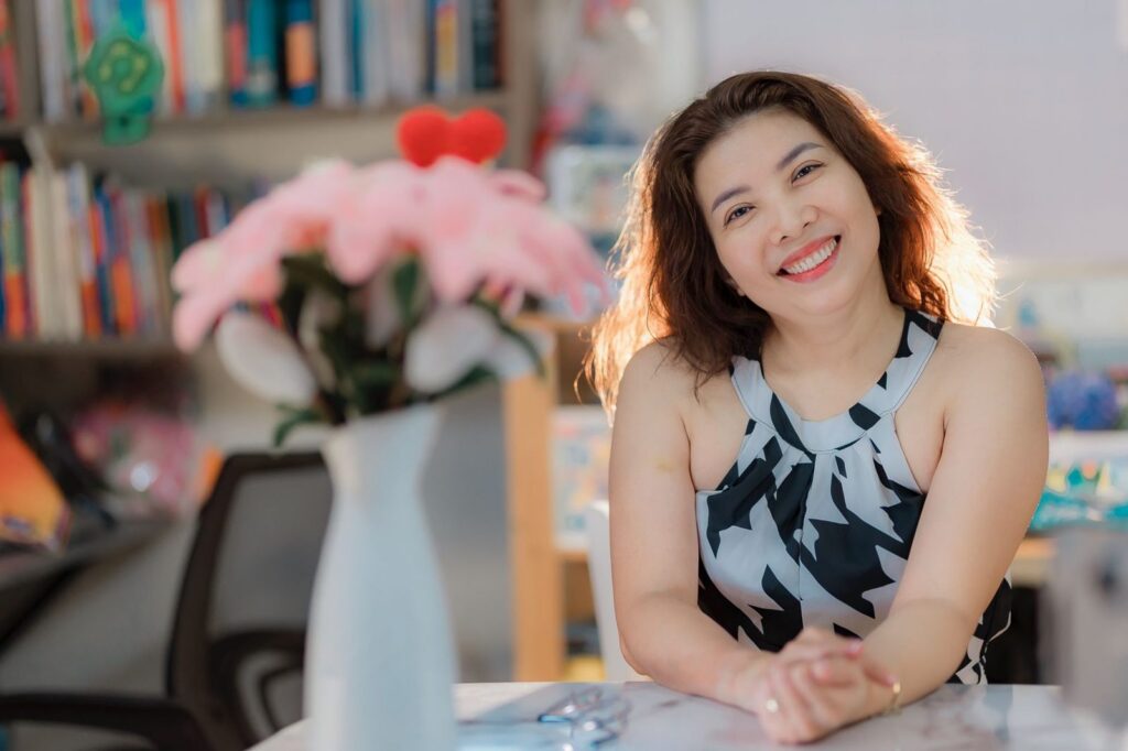 A smiling woman in her forties at home beside a vase of flowers