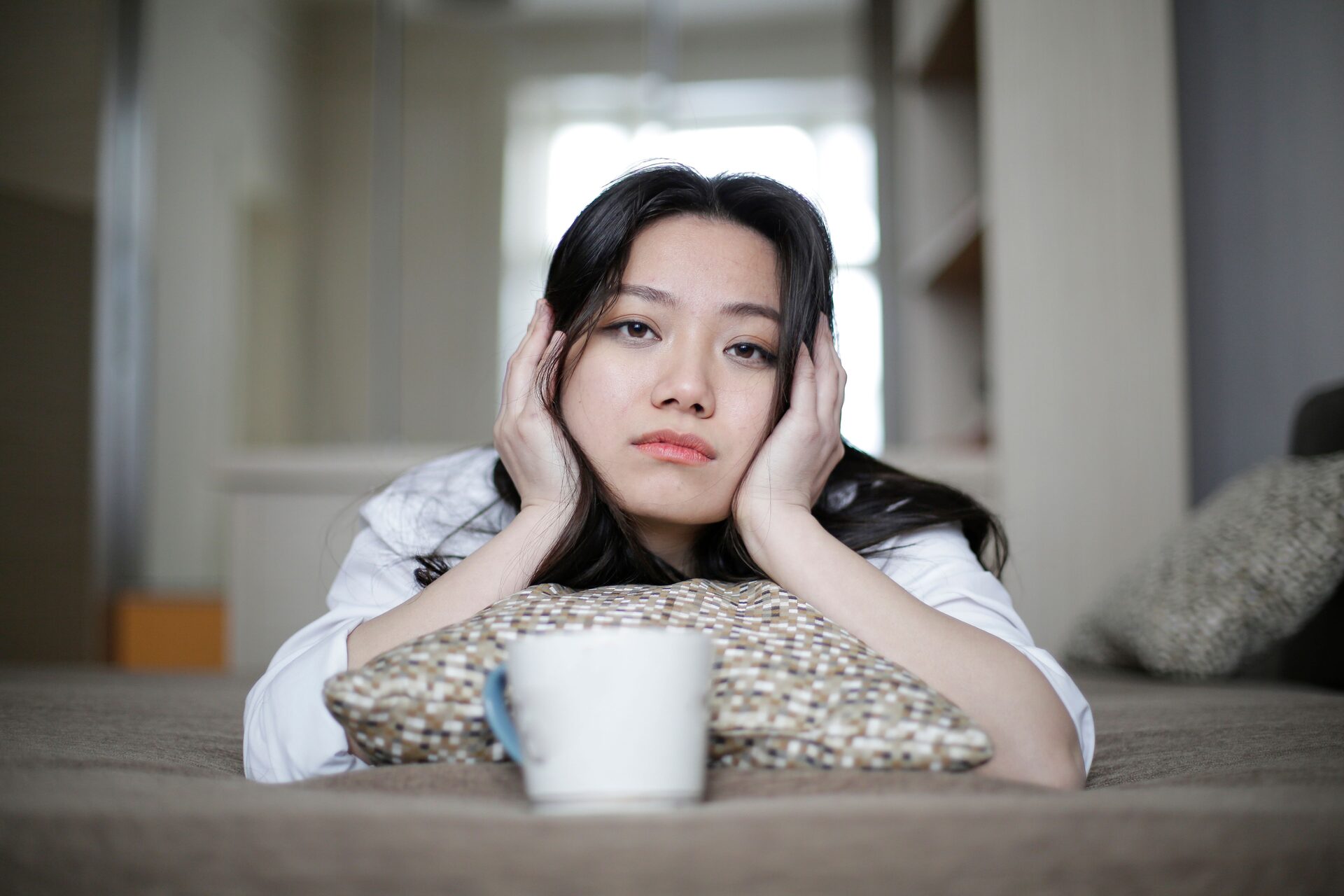 A young woman resting on a bed at home, looking tired